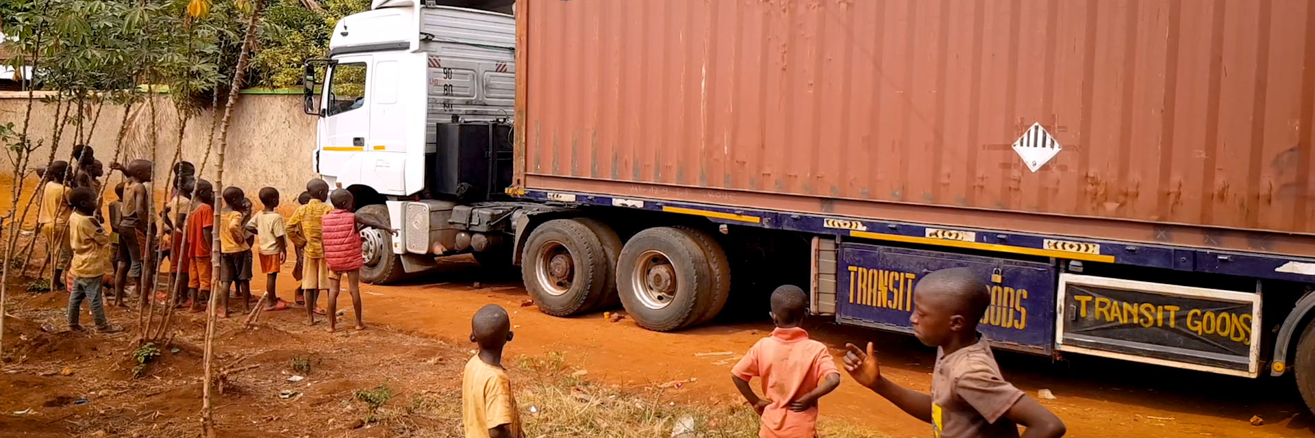 Photo of shipping container arriving at Ubuntu Clinique, with neighbourhood children watching nearby.